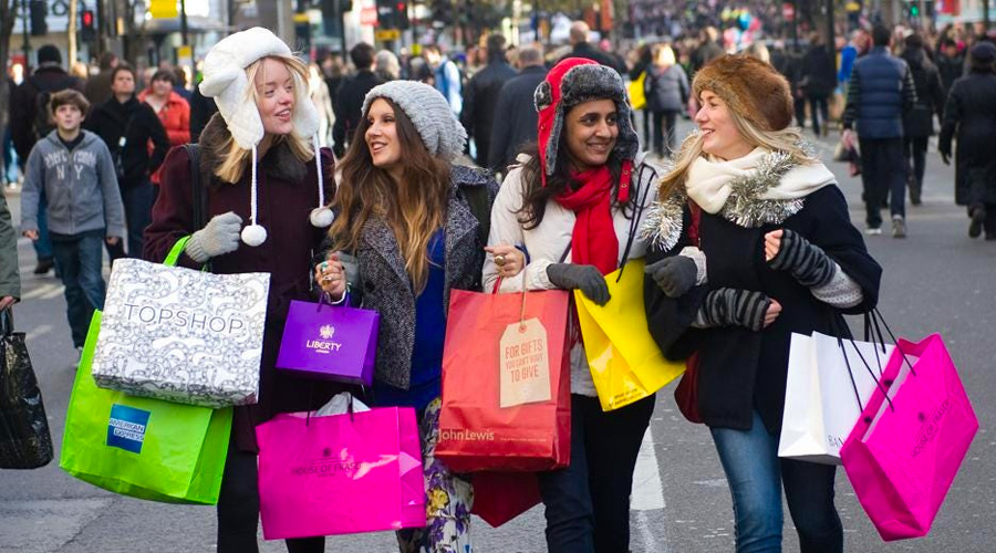 4 women holding shopping bags in the street smiling