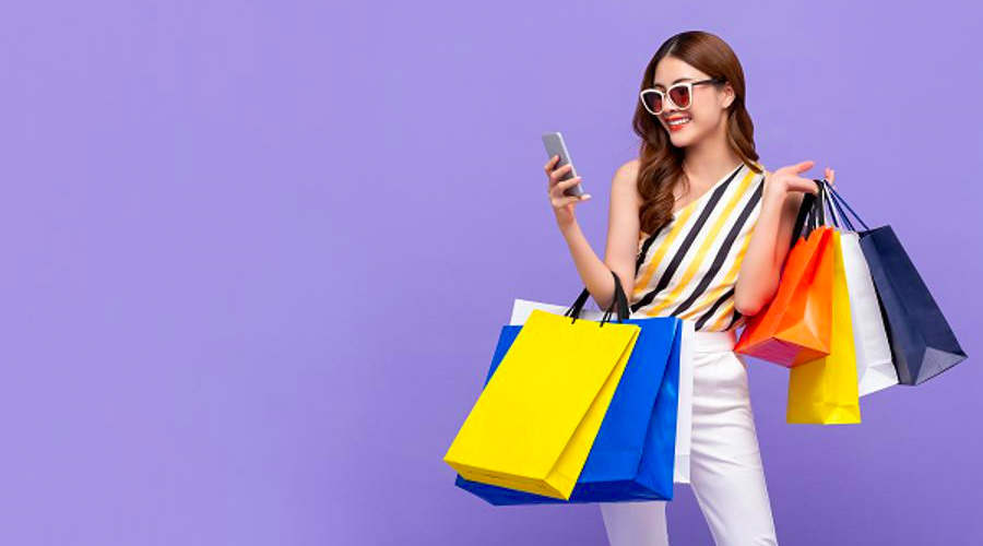 Woman in sunglasses holding shopping bags while on smart phone